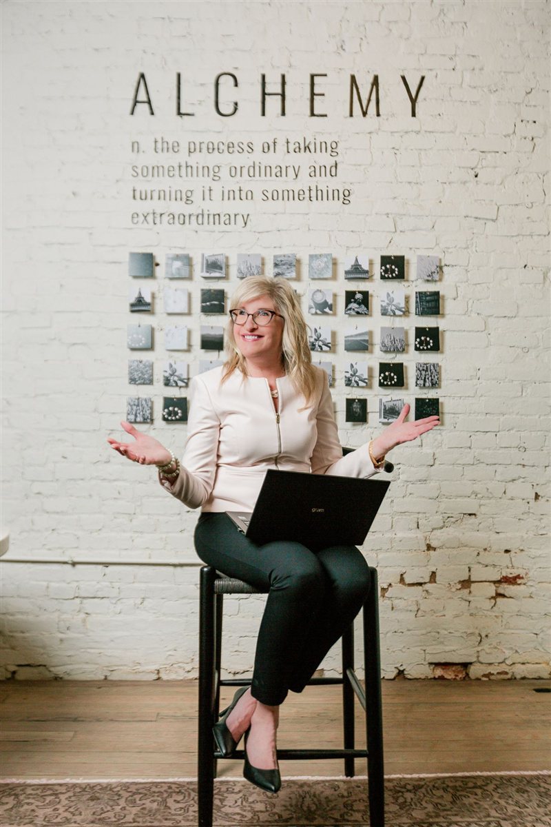 Mai White seated on a stool with a laptop, gesturing as she talks